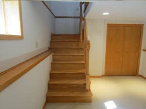 Newly constructed wooden stairs & railing lead to clean basement