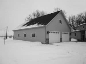 Snowy exterior of tall grey 2-stall garage with black roof