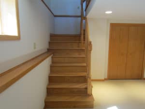 ‘After’ photo of newly built red oak stairs & railing leading to finished white & red oak basement