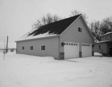 Snowy exterior of tall grey 2-stall garage with black roof
